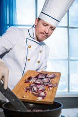 Wall Mural - Cook in white uniform puts sliced onions in the pan