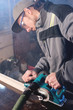© yanik88 - Young carpenter with a beard working with an electric plane with suction of sawdust. Leveling and sanding wooden bars