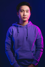 Portrait Of A Handsome Young Japanese Man, Dressed In Casual Wear. Not Emotional Guy Looking At Camera With Serious Face, Isolated At Studio Against Puple Wall