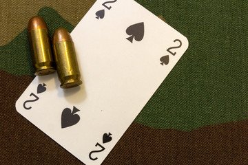 Two vintage pistol bullets and playing card on military camouflage seamless pattern background. Military gambling concept.