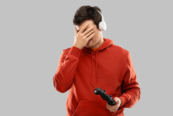 technology, gaming and people concept - young man or gamer in headphones with gamepad failed in video game