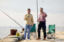 Leisure And People Concept - Happy Friends With Fishing Rods, Fish And Beer On Pier At Sea