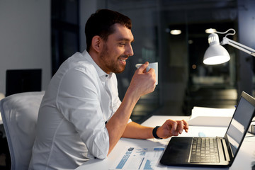 Canvas Print - business, deadline and people concept - smiling businessman with laptop computer working and drinking coffee at night office