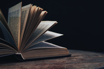 Aufkleber - One open old book on a round wooden table. Beautiful dark background...