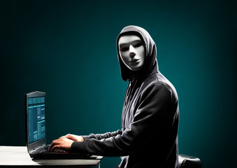 Wall Mural - Computer hacker in white mask and hoodie. Obscured dark face. Data thief, internet fraud, darknet and cyber security concept.