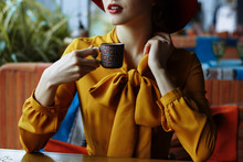 Portrait Of A Girl In A Cafe With A Cup Of Coffee And A Hat.portrait Of Sensual Young Girl Wearing Floppy Hat And Blouse With Bow. Beautiful Brunette Woman In Cafe Holding Cup Of Coffee