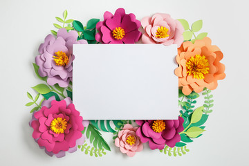 Poster - top view of white blank card on multicolored paper flowers with green leaves on grey background