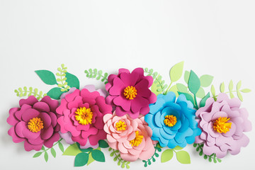 Sticker - top view of multicolored paper flowers and green leaves on grey background