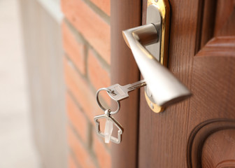 Key with house-shaped trinket in door lock, closeup. Space for text