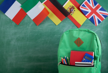 Fototapete - backpack, flags of Spain, France, Great Britain and other countries and school supplies on the background of the blackboard