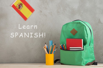 Fototapete - backpack, flag of the Spain and school supplies against a cement wall with text 