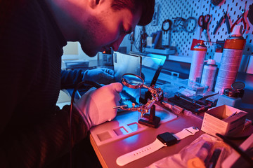 Wall Mural - The technician repairs a broken tablet computer in a modern repair shop. Illumination with red and blue lights