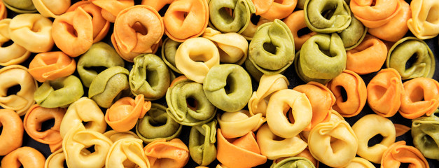 Uncooked colorful tortellini pasta texture background, banner