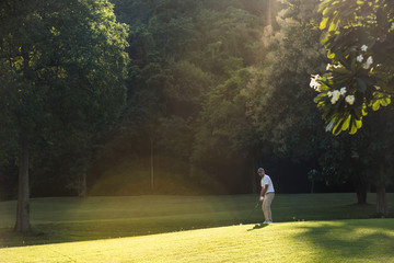 Wall Mural - Young Asian man playing golf on a beautiful natural golf course