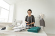 © satura_ - Dressmaker, fashion, tailor and people concept - young female fashion designer working in her showroom