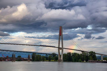 Beautiful view of Skytrain Bridge going over Fraser River during a cloudy evening with rainbow in the background. Taken in New Westminster, Vancouver, BC, Canada.