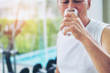 Wall Mural - Senior man drink mineral water in gym fitness center after exercise. Elderly healthy lifestyle.