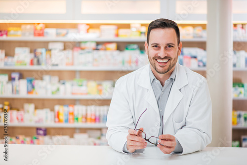 Fotomural Portrait of a cheerful handsome pharmacist leaning on counter at drugstore