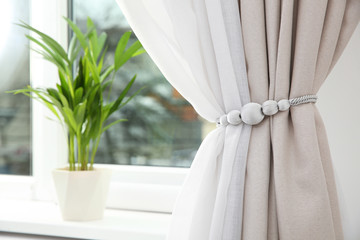 Draped window curtains with tieback in room, space for text. Home interior