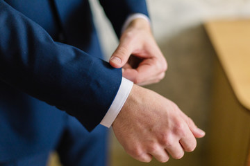 Businessman in a white shirt straightens cuffs, standing at the window in natural light. Man buttons cuff-link on French cuffs sleeves luxury white shirt. Concept successfully bisinesman