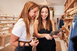 © Monkey Business - Two Female Friends Looking At Mobile Phone As They Shop In Independent Fashion Store