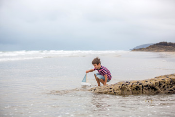 Canvas Print - Child plays with sand on beach. Cute preschool boy with toy ship on beach. Stormy seaside sgore and kid playing