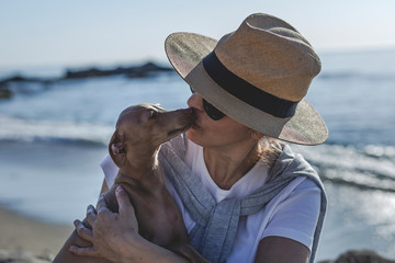 Beautiful brunette woman playing with dog on the beach