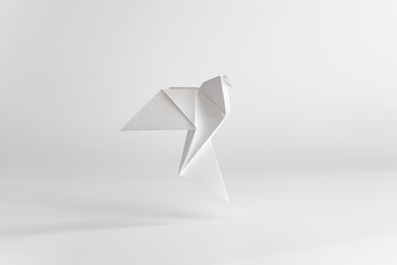 Origami dove made of white paper on white background. Minimal concept.