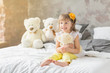 Portrait of child girl having fun sitting and playing with a teddy bears on a bed.