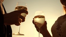 couple in love holding wine glasses with sparkling wine on background of sunset. close-up. teamwork of loving couple. celebrating success and victory. champagne sparkles and foams in sun. Slow motion