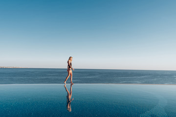 Wall Mural - girl in a swimsuit walks along the edge of the panoramic pool