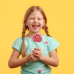 Wall Mural - Cute little girl licks candy and laughs in the studio on a yellow background