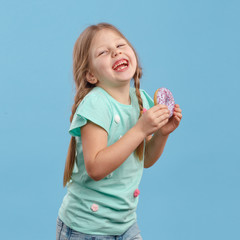 cute little girl eating a sweet donut and laughs in the studio on a blue background