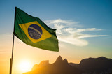 Fototapeta Tęcza - Brazilian flag waving backlit in front of the golden sunset mountain skyline at Ipanema Beach in Rio de Janeiro, Brazil