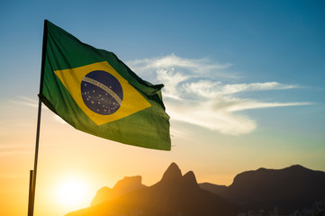 brazilian flag waving backlit in front of the golden sunset mountain skyline at ipanema beach in rio
