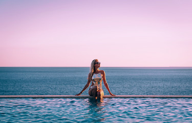 Wall Mural - girl in a swimsuit near the panoramic pool on the background of the sea relaxes