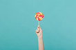 Close up female holding in hand colorful round lollipop isolated on blue turquoise wall background. Proper nutrition or sweets dessert fast food, dieting morning concept. Copy space for advertisement.