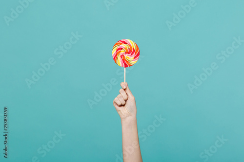 Close up female holding in hand colorful round lollipop isolated on blue turquoise wall background Poster Mural XXL