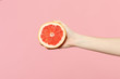 © ViDi Studio - Close up cropped photo of female hold in hand fresh ripe half grapefruit fruit isolated on pink pastel wall background. Copy space advertising mock up. People vivid lifestyle, relax vacation concept.