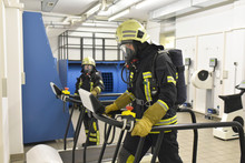 Two Firefighters With Respirator And Air Tank Exercising In Exercise Room