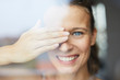 © Westend61 - Portrait of laughing young woman behind windowpane covering her eye