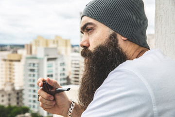 Wall Mural - Stylish bearded man smoking pipe looking at the horizon from the top of a tall building.