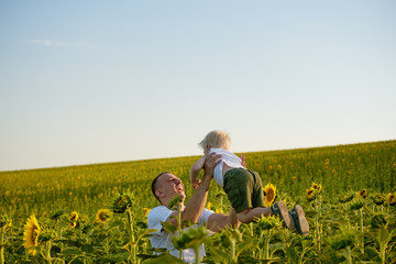 Wall Mural - Father throws up his little son on a green sunflowers field against the sky.