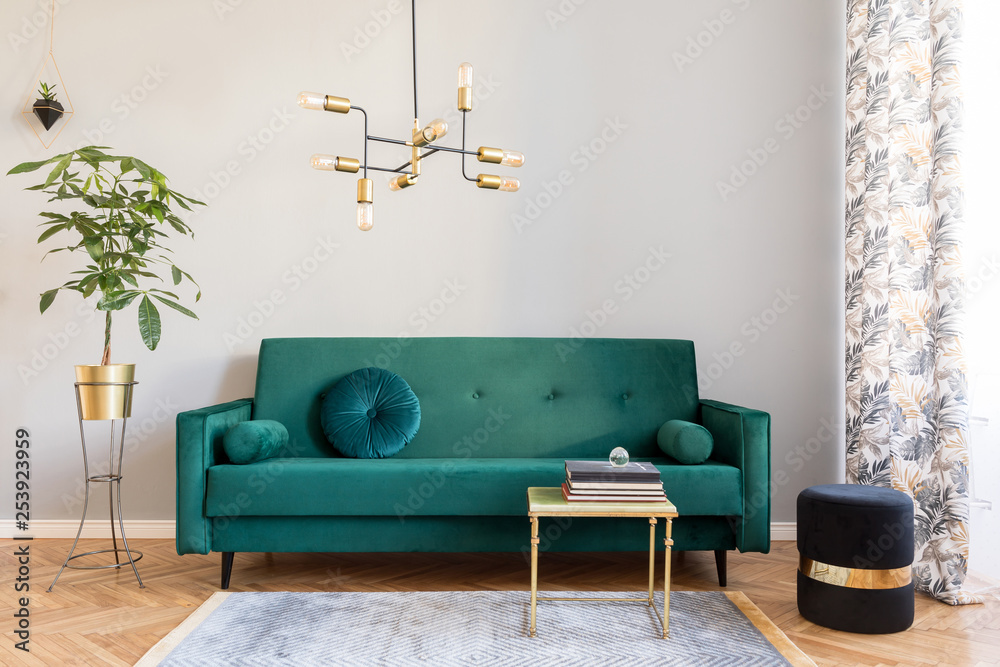 Bright and sunny minimalistic home interior with design green velvet sofa, furniture,plant, gold coffee table with books and elegant pendant lamp. Brown wooden parquet. Stylish decor of living room. - obrazy, fototapety, plakaty 