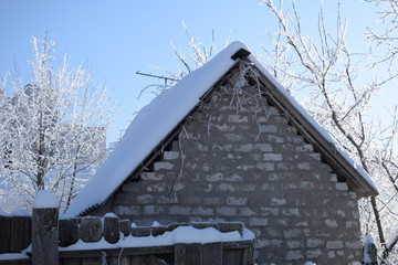 Snow covered tree branches above the snowy roof of a brick building with a blue sunny sky