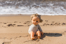 Old Broken Toy Doll Sitting On A Beach In Italy
