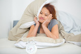 Fototapeta Psy - woman in bed looking ruefully at alarm clock