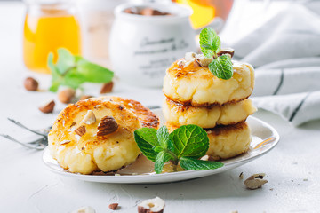 Wall Mural - Breakfast Food Delicious Concept. Cottage cheese pancakes, syrniki, curd fritters with honey and huts on white concrete table background. Close-up