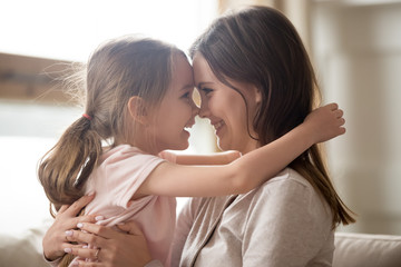 Wall Mural - Cute kid girl embracing smiling mom touching noses having fun