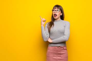 Woman with glasses over yellow wall thinking an idea pointing the finger up